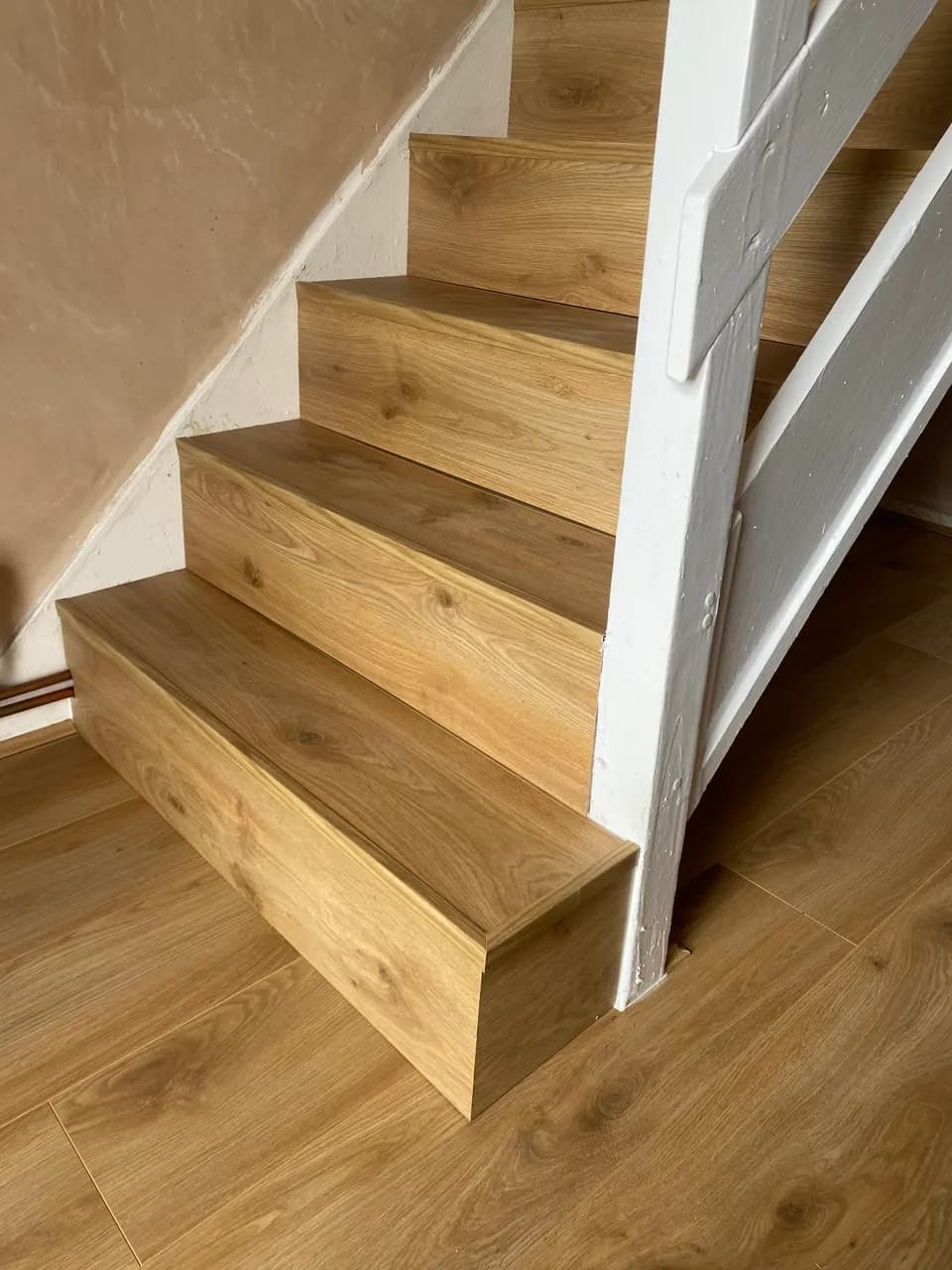 Light oak laminate on the bottom steps of a staircase, matching the floor below, with a white-painted string