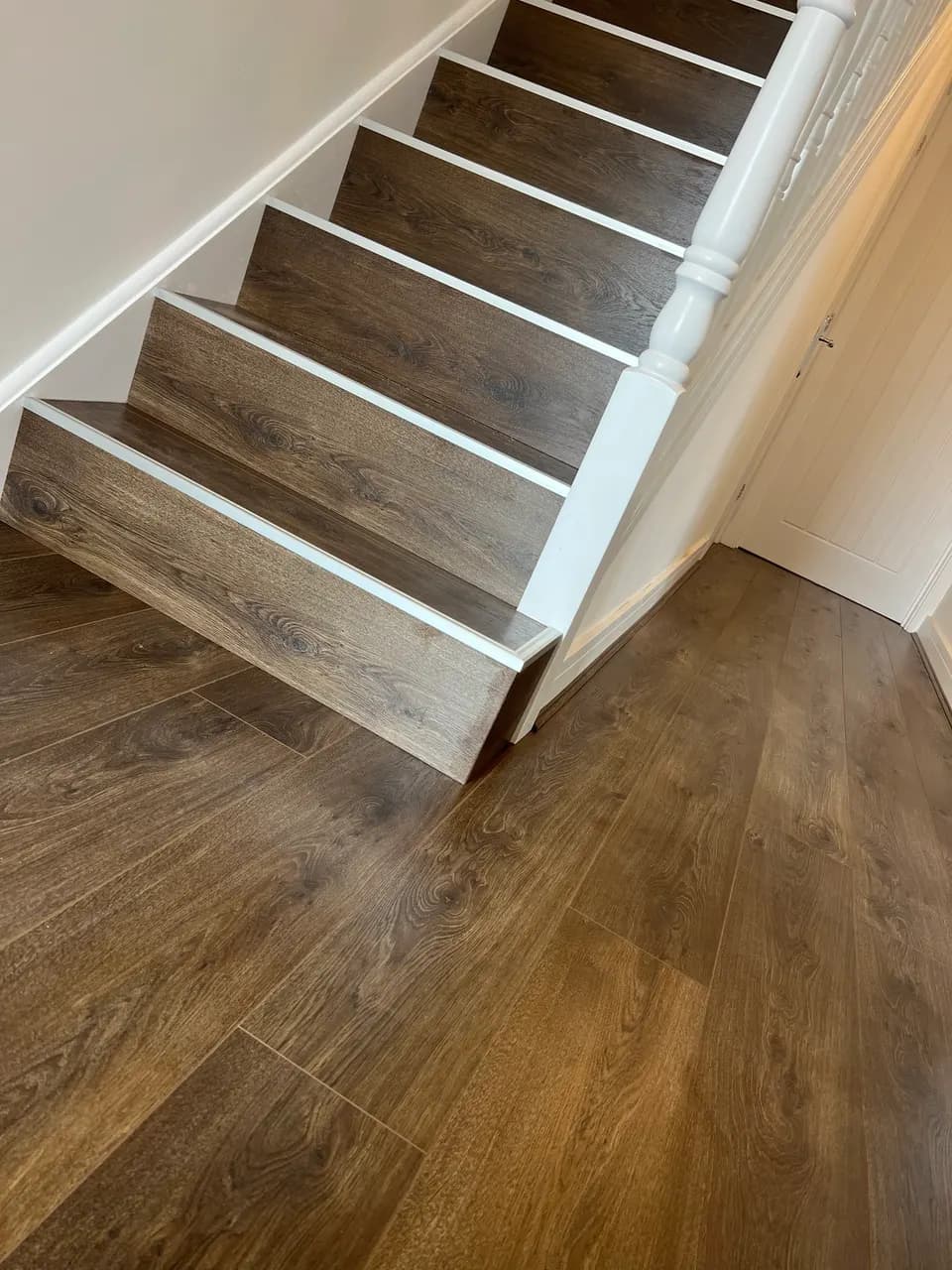 Dark oak laminate stairs with white nosings, running down onto a matching hallway floor