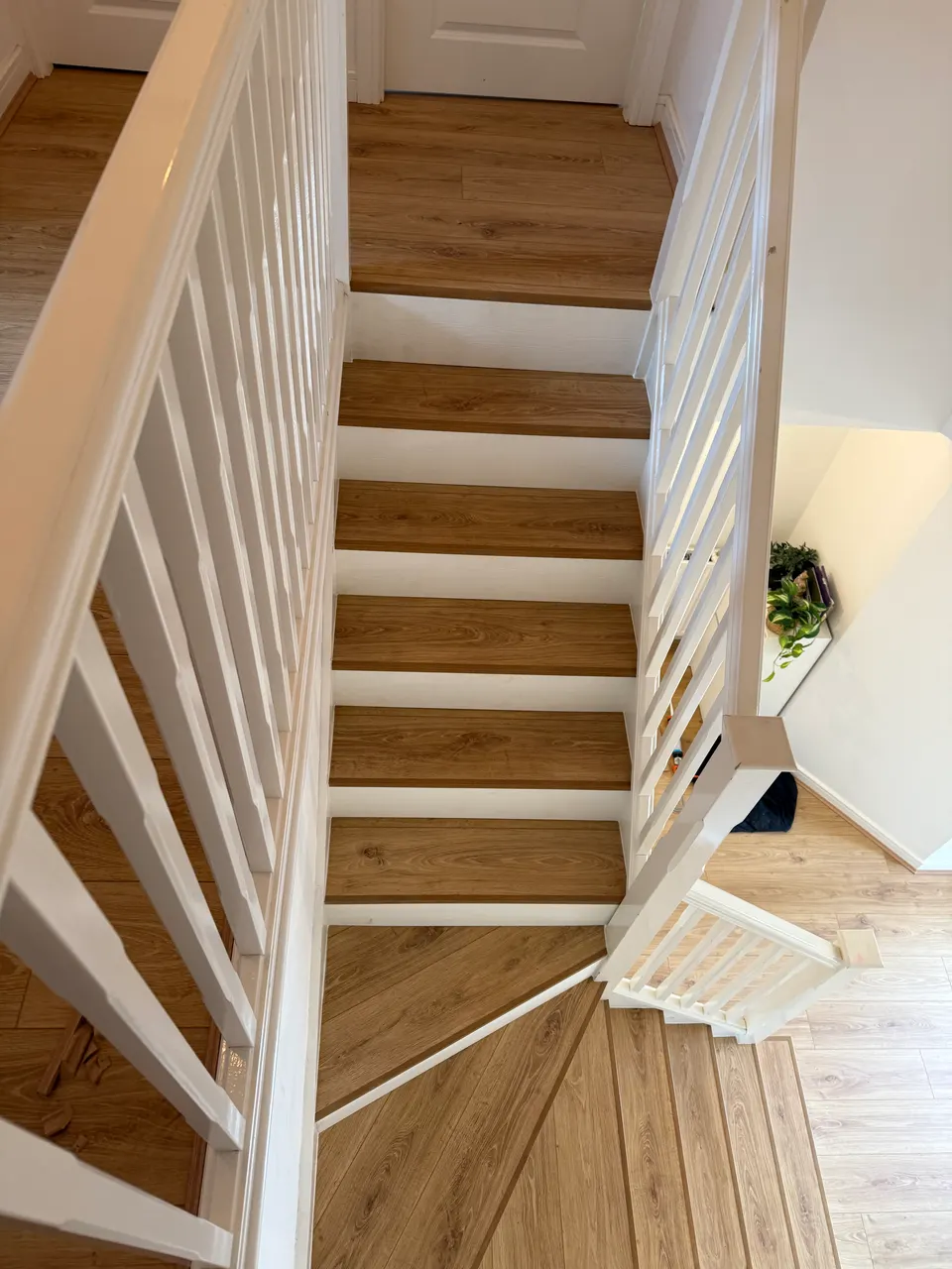 Looking down a light oak laminate staircase with white spindles, turning at the bottom