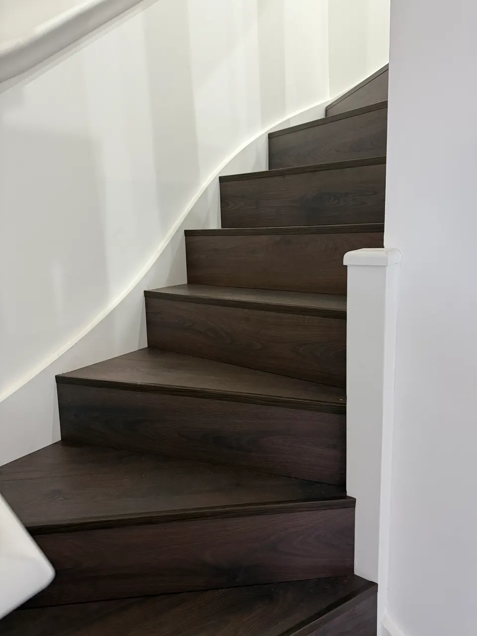 Dark walnut-toned laminate on a curved staircase with a white-painted wall