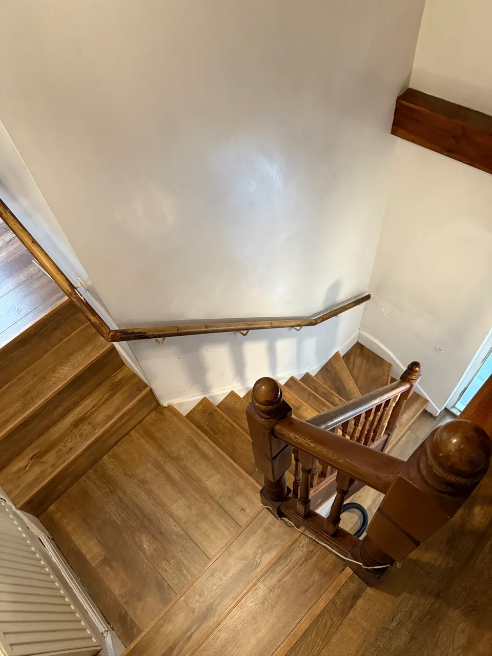 Looking down a mid-oak laminate staircase with a dark wooden handrail and newel post