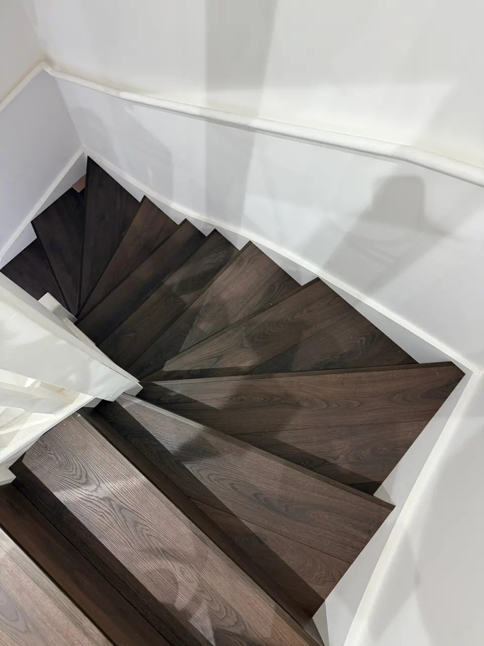 Looking down onto dark laminate winder steps turning a corner between white walls