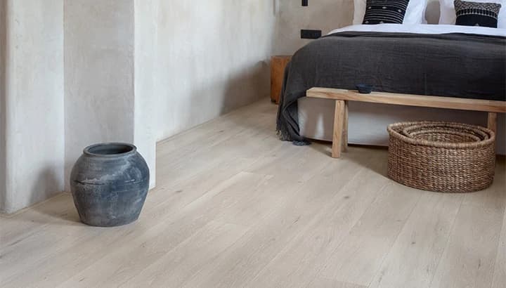 Pale oak laminate plank flooring in a bedroom, with a bench and basket at the foot of the bed