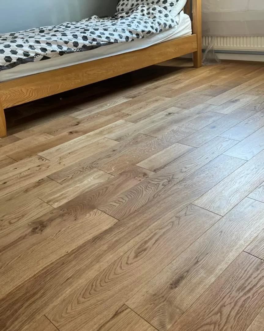 Engineered oak boards laid across a bedroom floor beside an oak bed frame